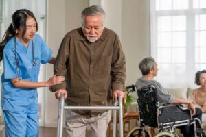 Older adult using a hallway handrail while staff member checks an emergency call system in an assisted living community